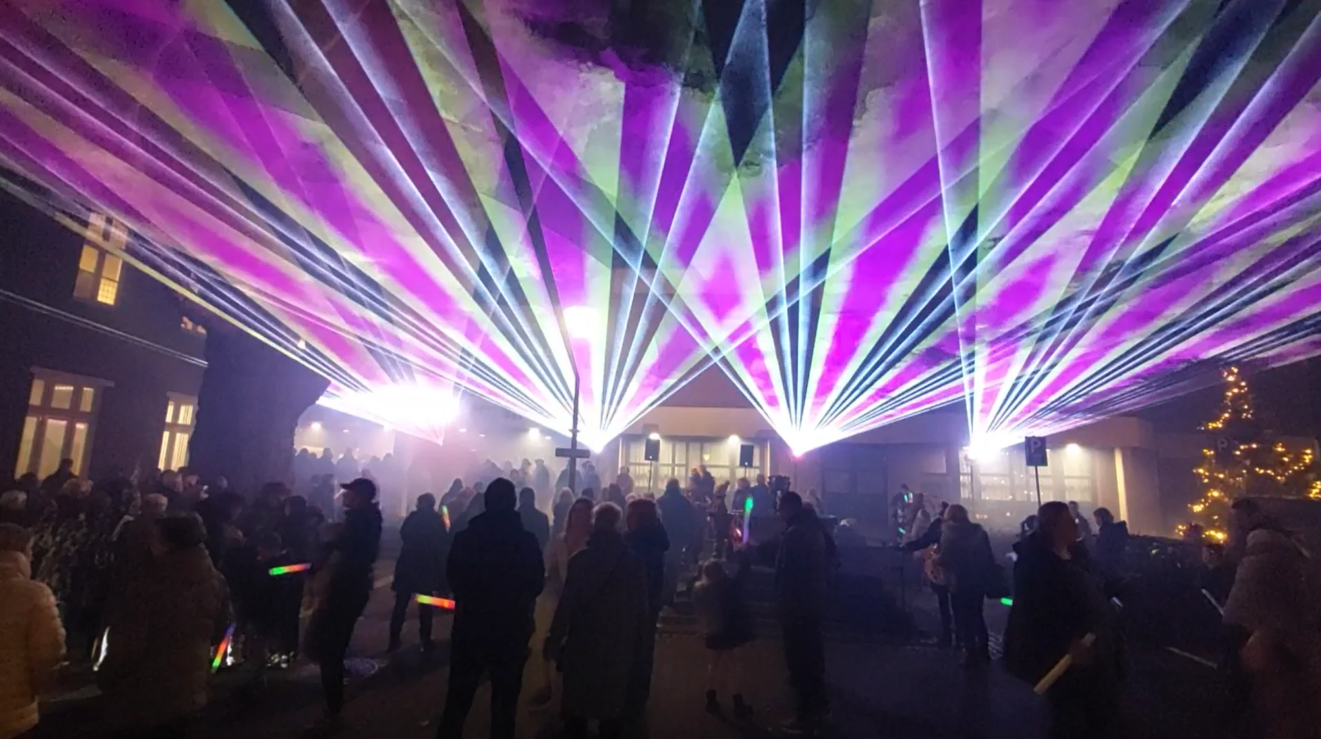 nebulaser-laser-show-belgie-nederland-gemeentehuis-paars nebulaser plein voor een gemeentehuis met publiek en vier laserprojectoren die paars en gele laserstralen projecteren