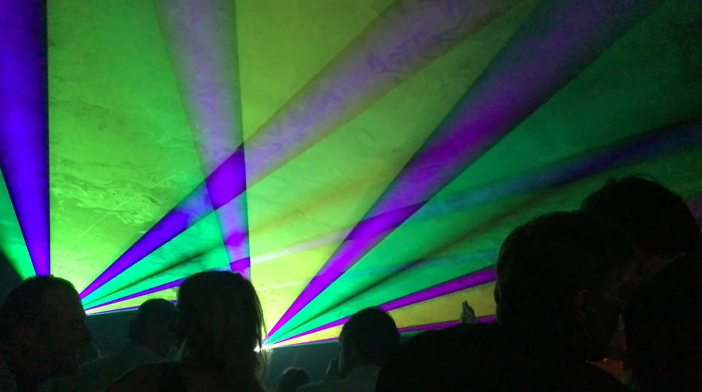 nebulaser-laser-show-belgie-nederland-statief-lasers-verjaardag-paars-geel-groen nebulaser zaal met twee laserprojectoren die paars en groene stralen projecteren, publiek op de voorgrond